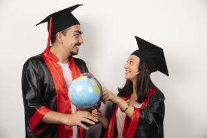 Two international graduates in the USA wearing black and red graduation gowns, smiling and holding a globe, symbolizing global education opportunities and career prospects.