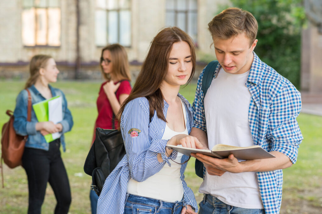 Student Life Hacks: Young students studying together outdoors, sharing notes and discussing coursework in a campus setting.