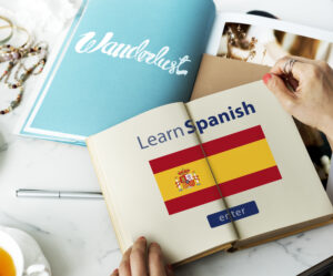 A person holding an open book with the Spanish flag and the words "Learn Spanish" on the page, representing online education and language learning.