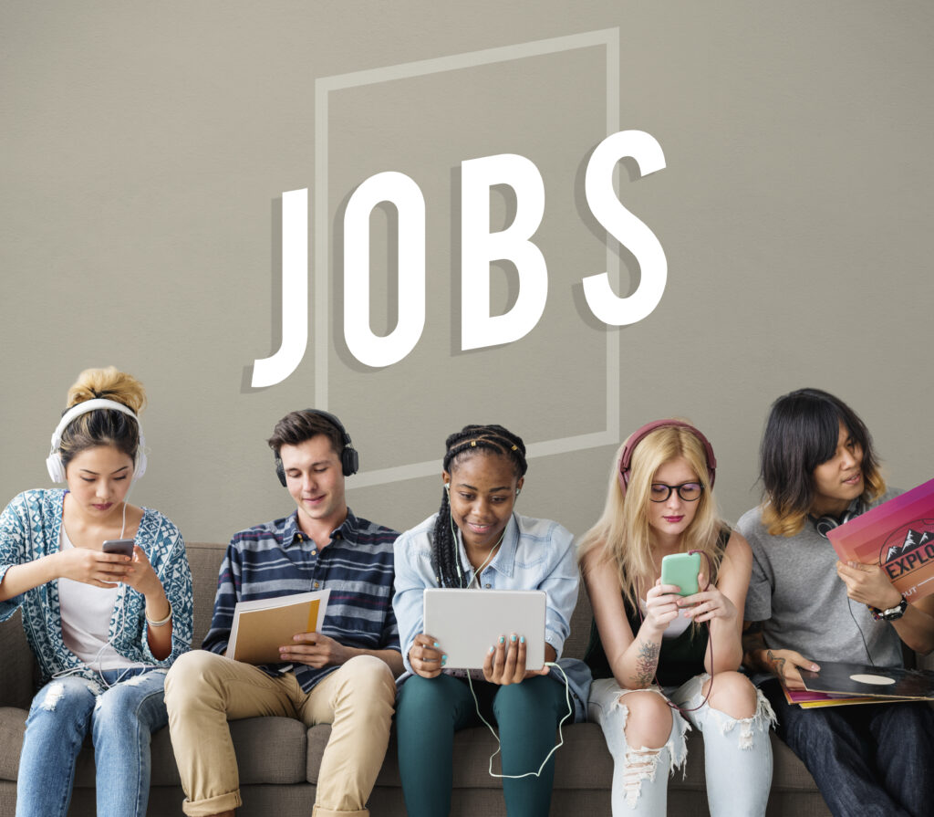Group of diverse young professionals sitting on a couch using digital devices, with the word 'JOBS' displayed in the background, representing job opportunities in Canada.