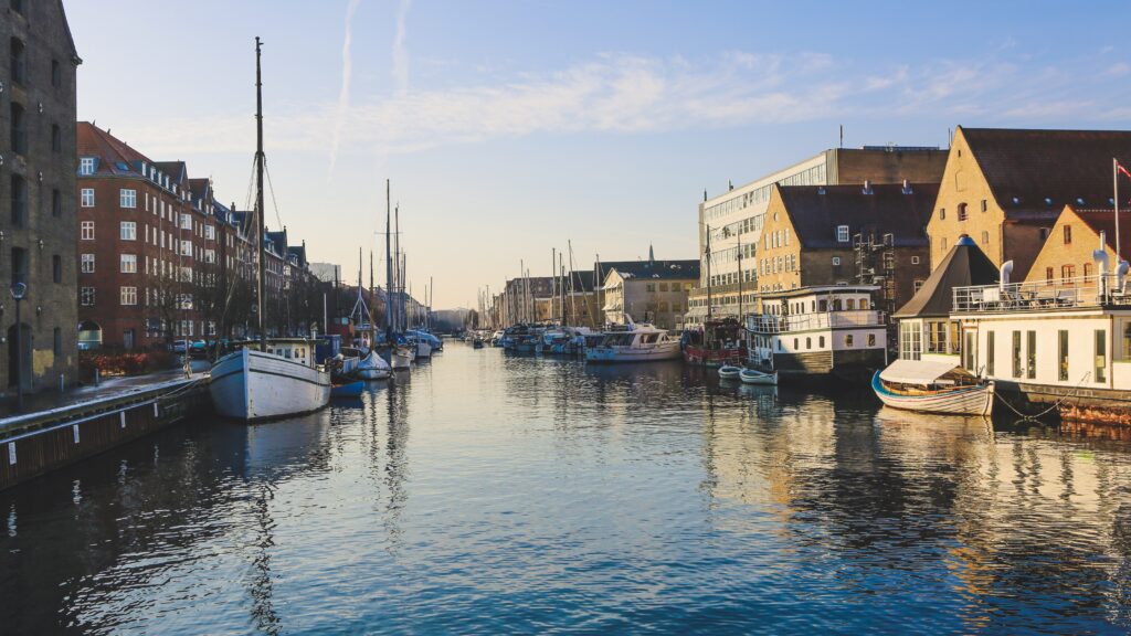 Scenic view of boats docked along a canal in Christianshavn, Copenhagen, Denmark, with historic and modern buildings, representing the experience of thriving in Denmark.