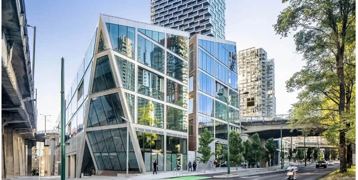 Modern glass building of University Canada West in downtown Vancouver, featuring angular architecture and reflective windows, with people walking and traffic passing on the street.