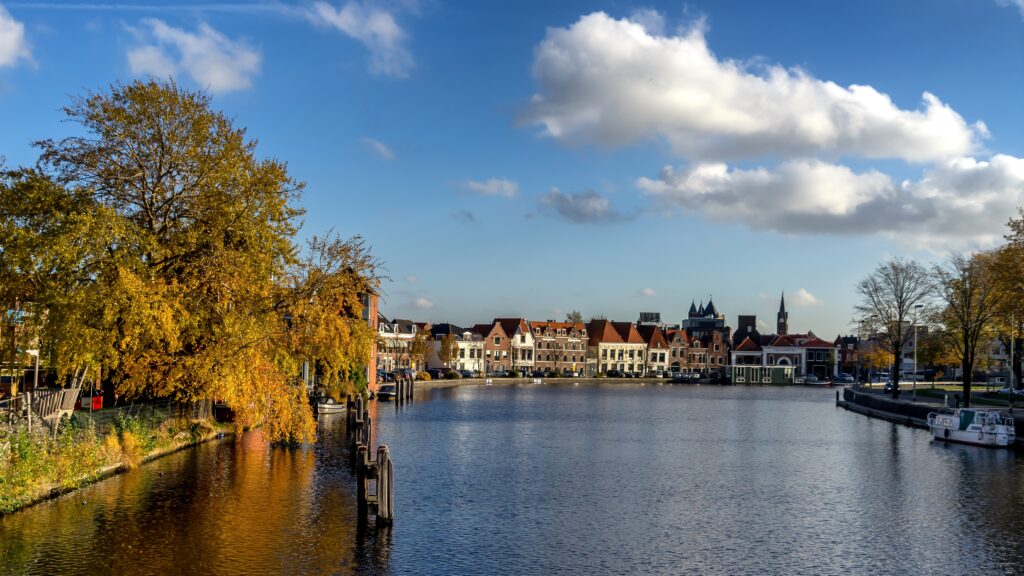 Scenic view of the Spaarne River in Haarlem, Netherlands, with traditional Dutch houses and autumn trees along the waterfront, representing a peaceful environment ideal for international students.