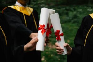 Three graduates hold diplomas tied with red ribbons, celebrating their achievement.