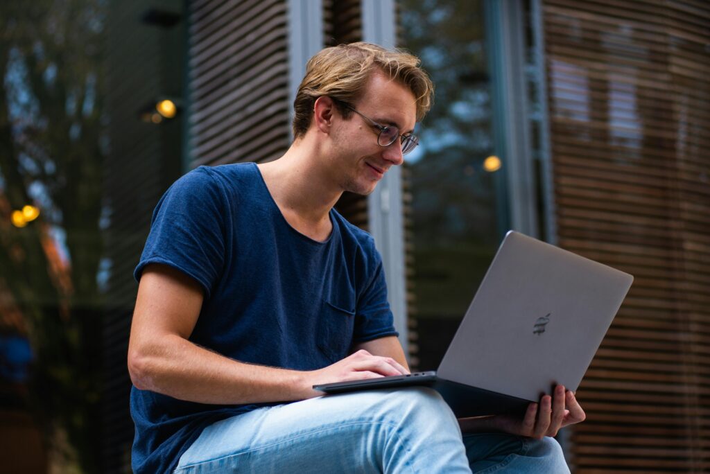 Young man in glasses working on laptop outdoors
