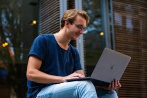 Young man in glasses working on laptop outdoors