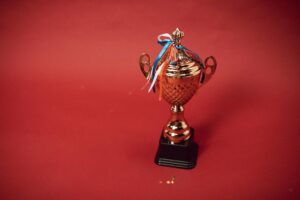 Gold trophy with blue, white, and orange ribbons on red background