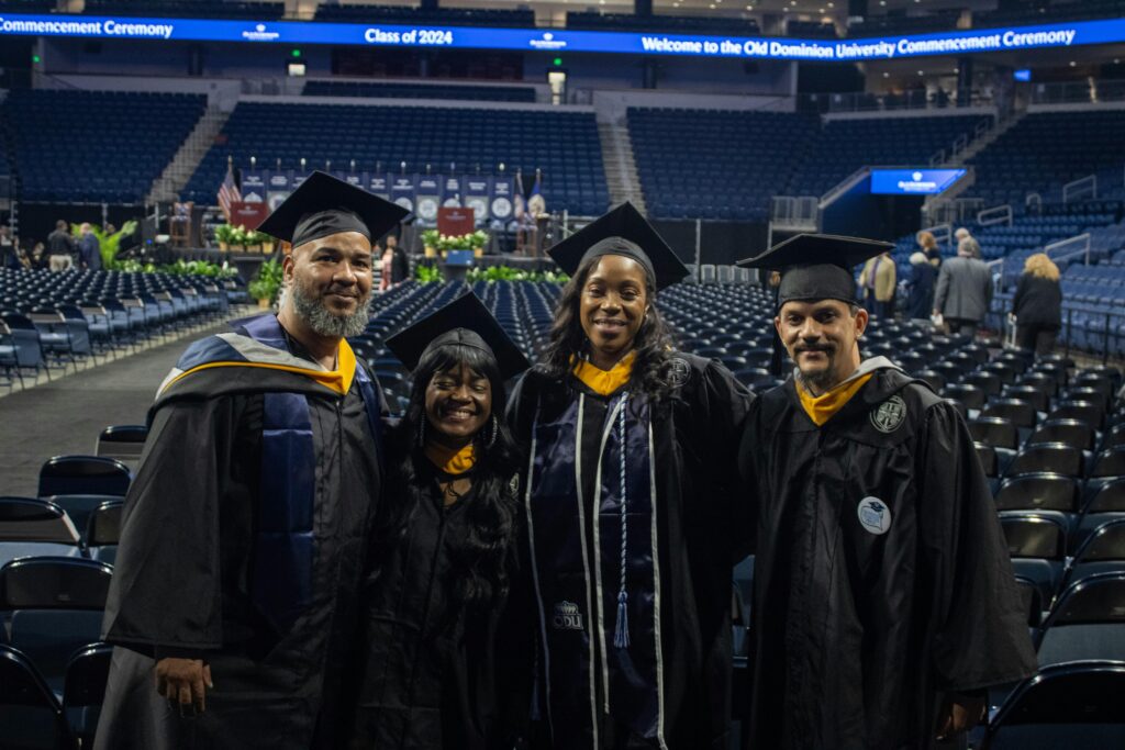 Four smiling Old Dominion University graduates in caps and gowns at their commencement ceremony.