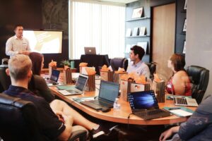 Students attending a digital marketing classroom session, listening to a presentation on digital marketing strategies while using laptops in a university seminar room.