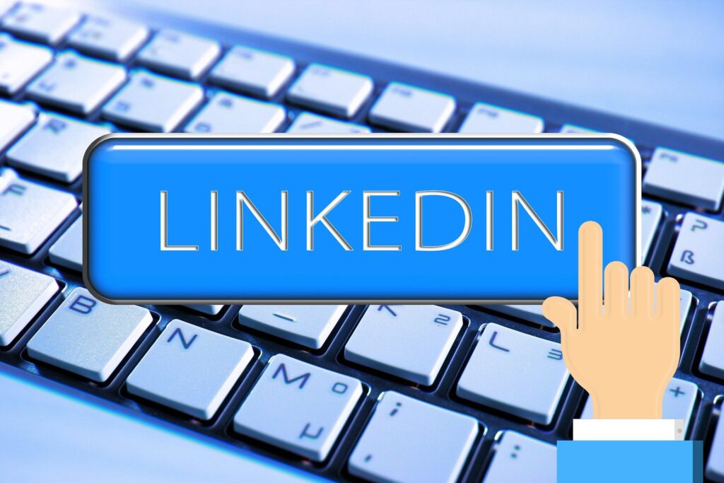 Blue LinkedIn button displayed on a computer keyboard with a hand cursor icon, representing online networking and professional connections.
