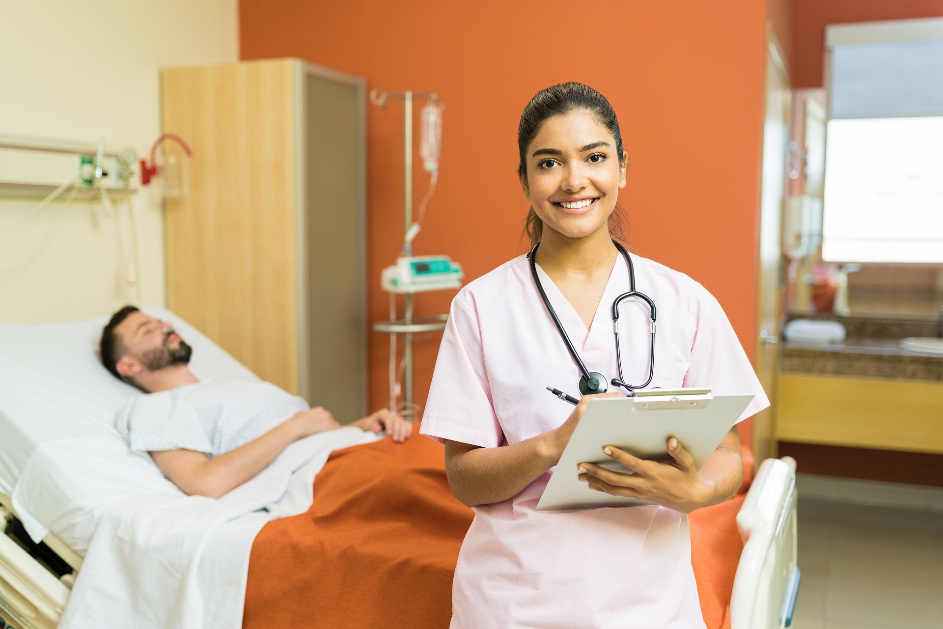 Nursing student in hospital setting holding a clipboard with a patient resting in bed during clinical training, representing hands-on nursing education abroadNursing student in hospital setting holding a clipboard with a patient resting in bed during clinical training, representing hands-on nursing education abroad