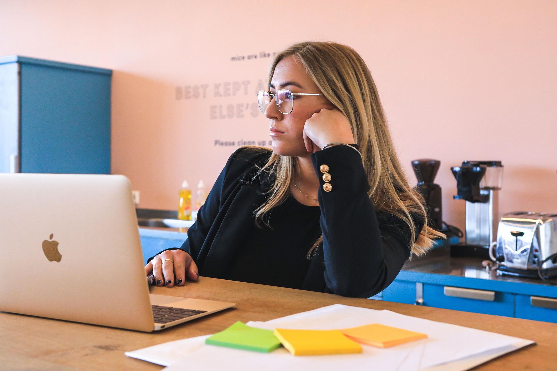 Student sitting at a desk using a laptop with notes and sticky pads, focused on studying in a modern workspace.