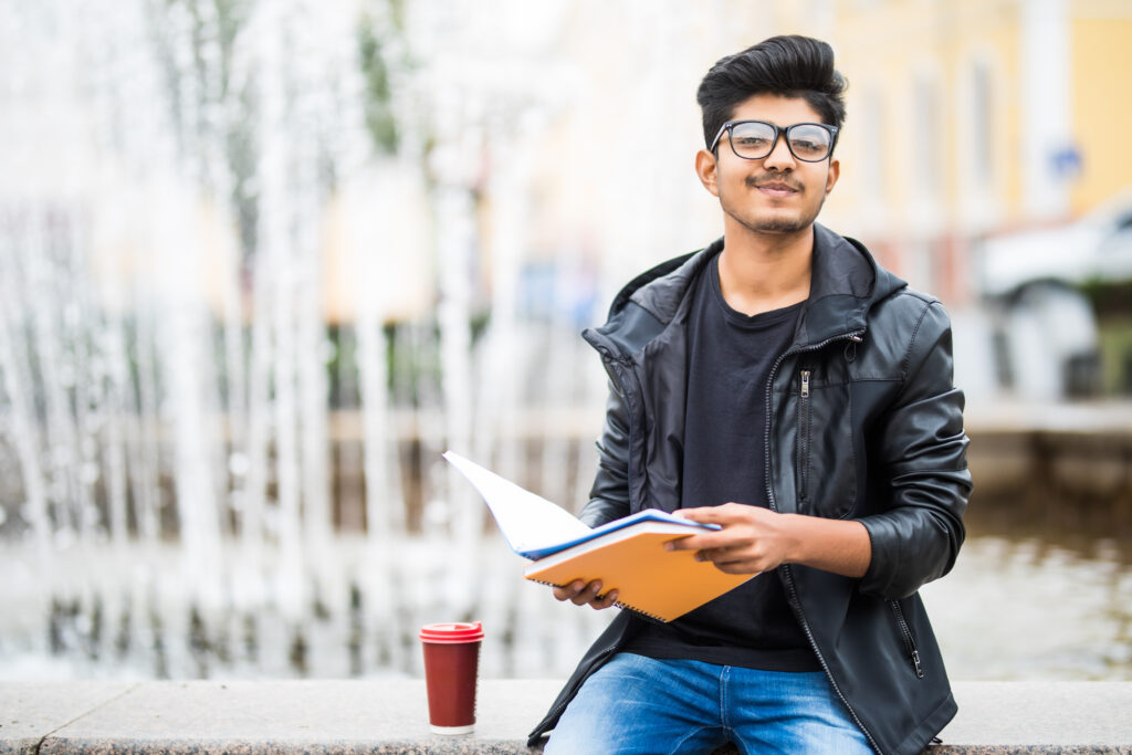Medical student holding study materials while sitting on a university campus, representing graduates preparing to transfer their medical qualifications back to Southeast Asia after completing an international medical degree.