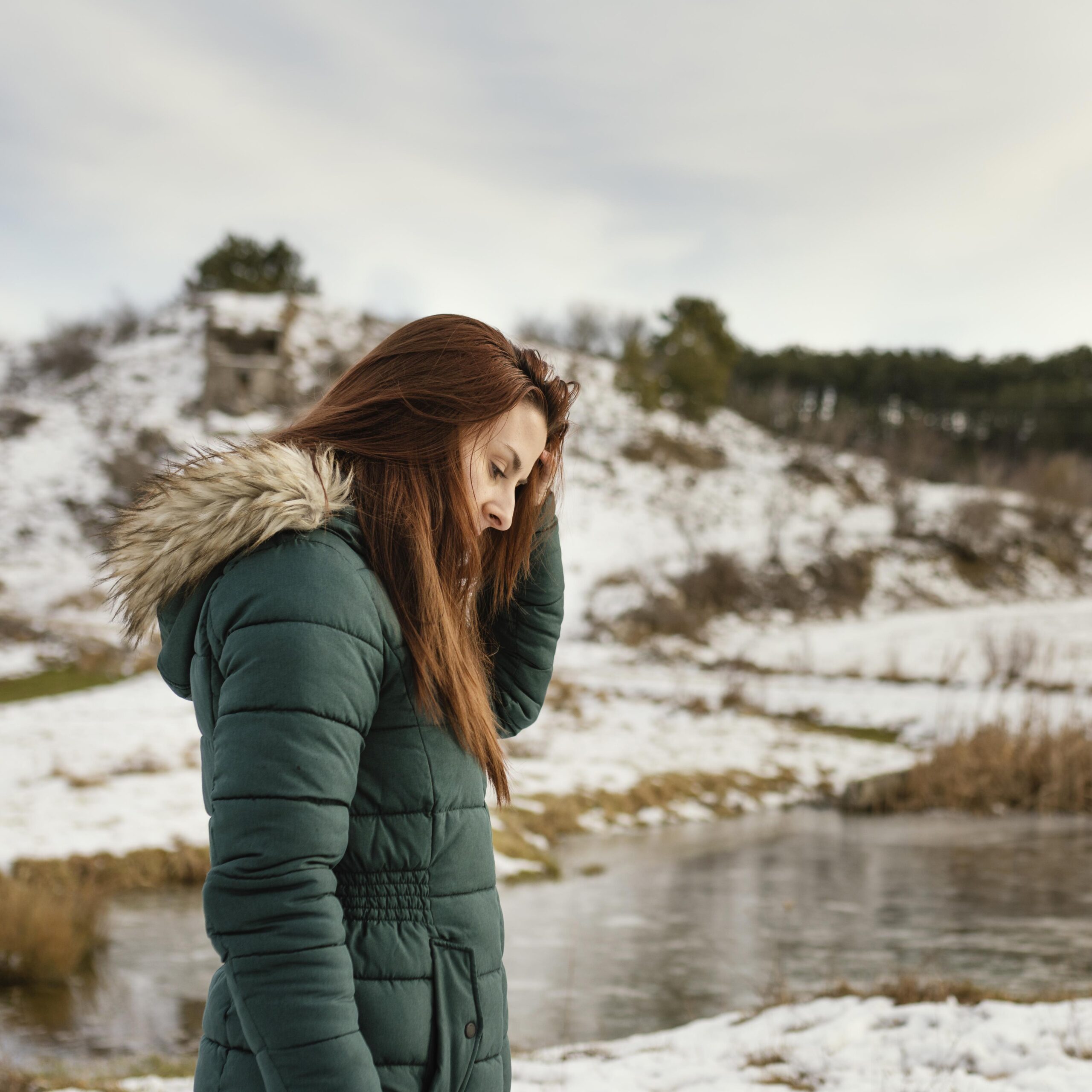 Young woman standing beside a snowy lake in winter, illustrating the emotional challenges of Seasonal Affective Disorder (SAD) and the importance of protecting mental health during long winter months abroad.