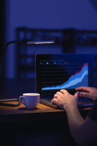 Data science professional analyzing a rising data chart on a laptop in a dark workspace, with a coffee cup beside the computer.