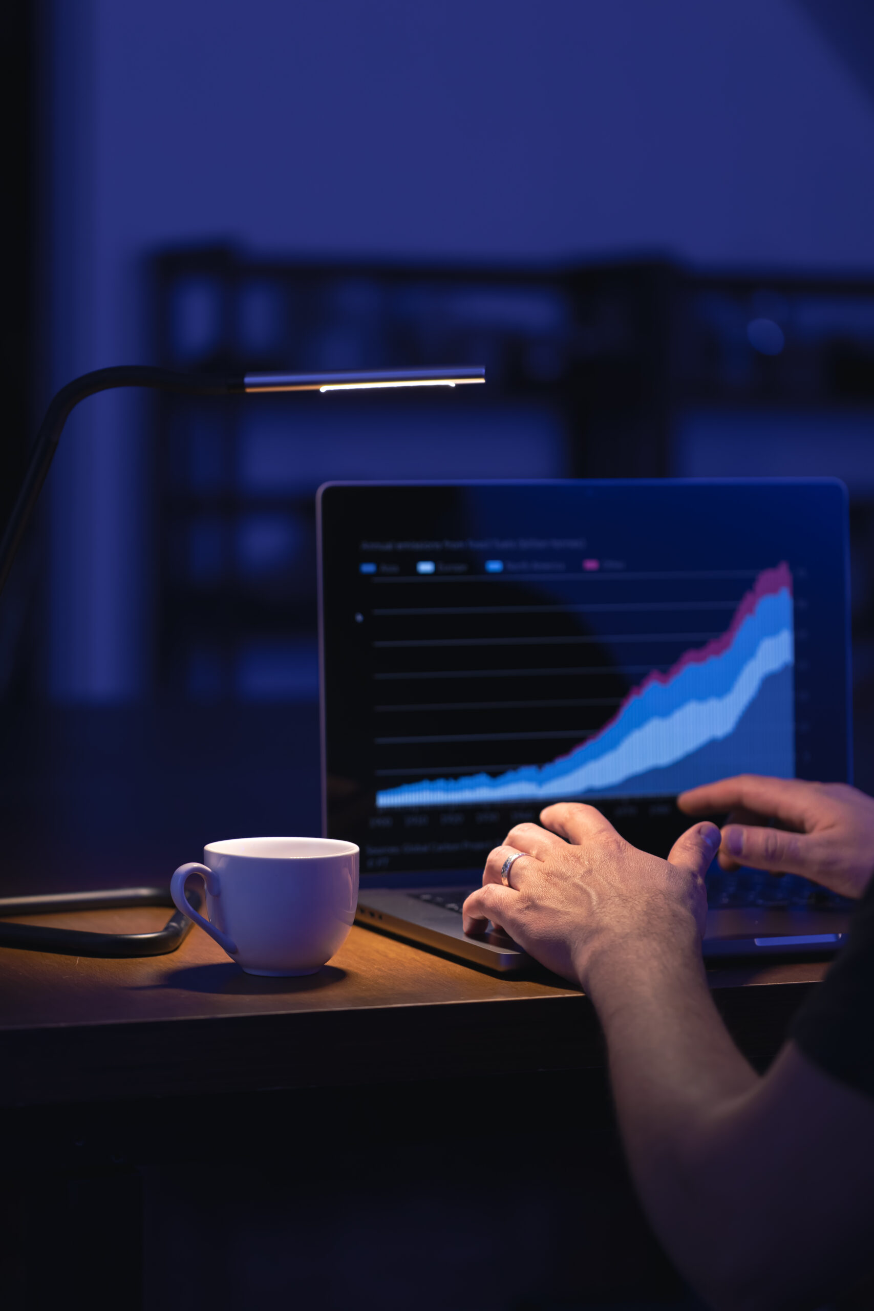 Data science professional analyzing a rising data chart on a laptop in a dark workspace, with a coffee cup beside the computer.