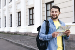 Smiling traveler holding a map while standing on a city street with a backpack.