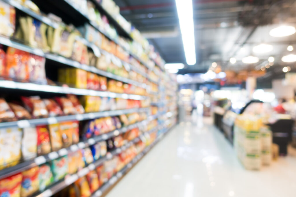 Blurred view of a brightly lit supermarket aisle with shelves stocked with colorful products.