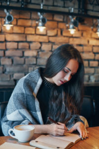 Student studying and writing in a notebook with a cup of coffee at a cozy café table.
