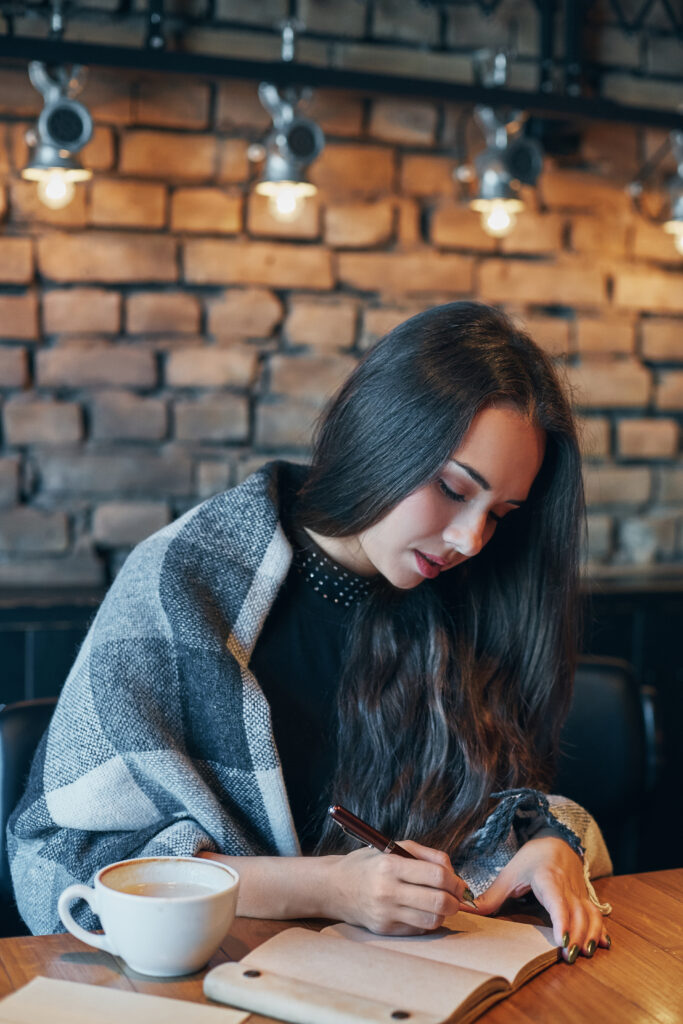 Student studying and writing in a notebook with a cup of coffee at a cozy café table.