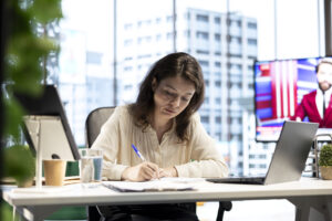 International student studying business at a desk with a laptop and notebook in a modern office setting.