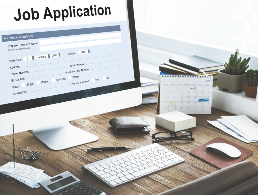 Job application form displayed on a computer monitor at a desk with office supplies and a calendar.