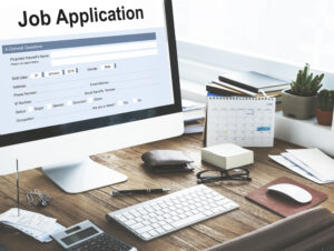 Job application form displayed on a computer monitor at a desk with office supplies and a calendar.