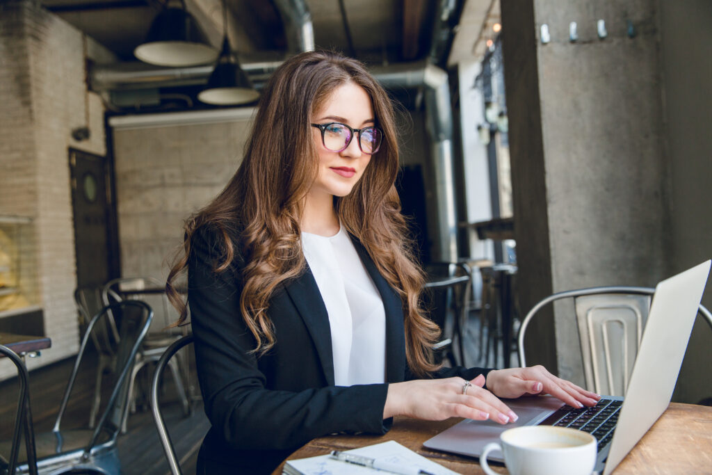 Professional businesswoman working on a laptop while sitting at a café table with a cup of coffee.